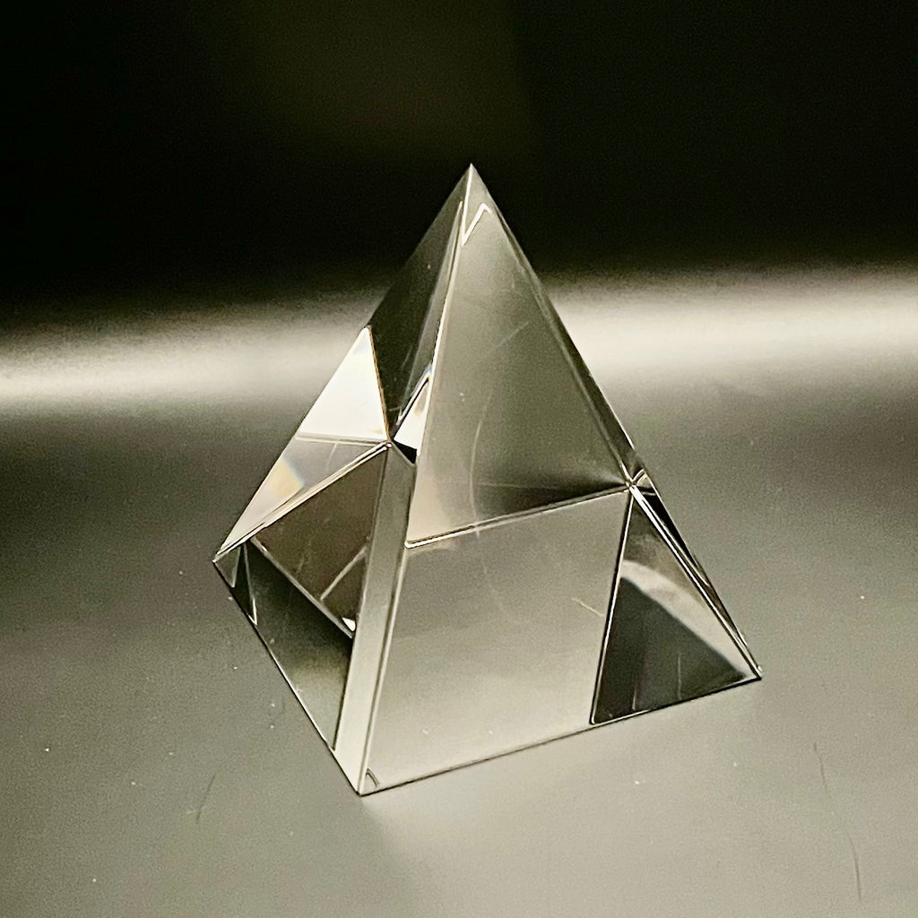 Clear glass pyramid on a reflective surface with a dark background