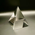 Clear glass pyramid on a reflective surface with a dark background