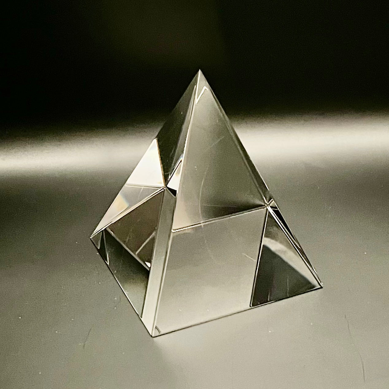 Clear glass pyramid on a reflective surface with a dark background