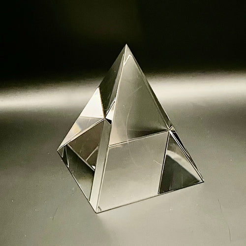 Clear glass pyramid on a reflective surface with a dark background