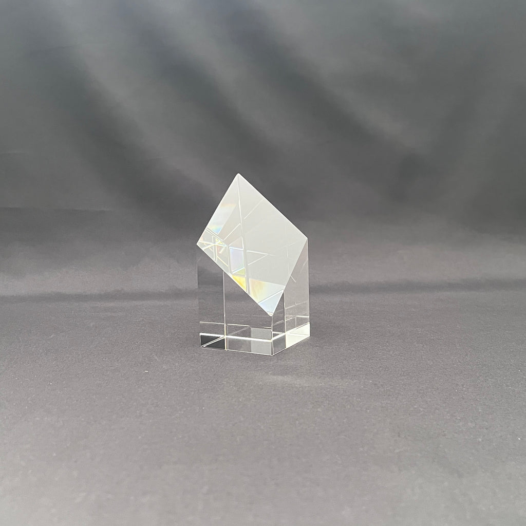 A clear crystal or glass geometric crystal tower with a diamond-shaped top and a square base.