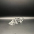 A clear, transparent miniature truck and trailer model, made of crystal, displayed on a dark gray surface against a black background.