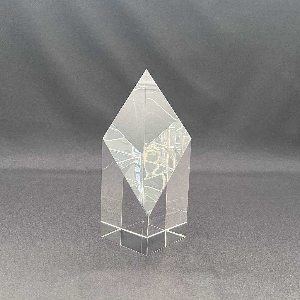 A clear acrylic or glass geometric crystal award tower with a diamond-shaped top and a square base, 
