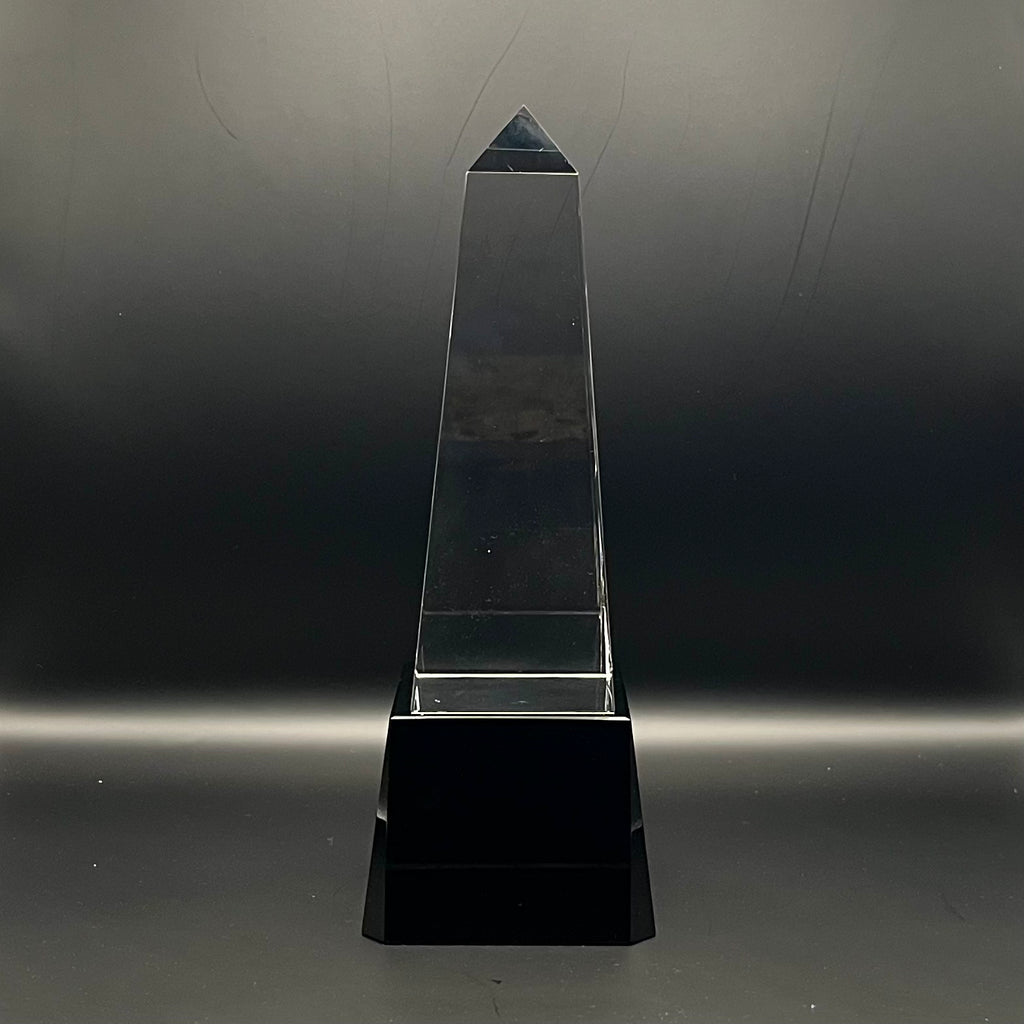 Clear crystal obelisk on a black base against a dark background
