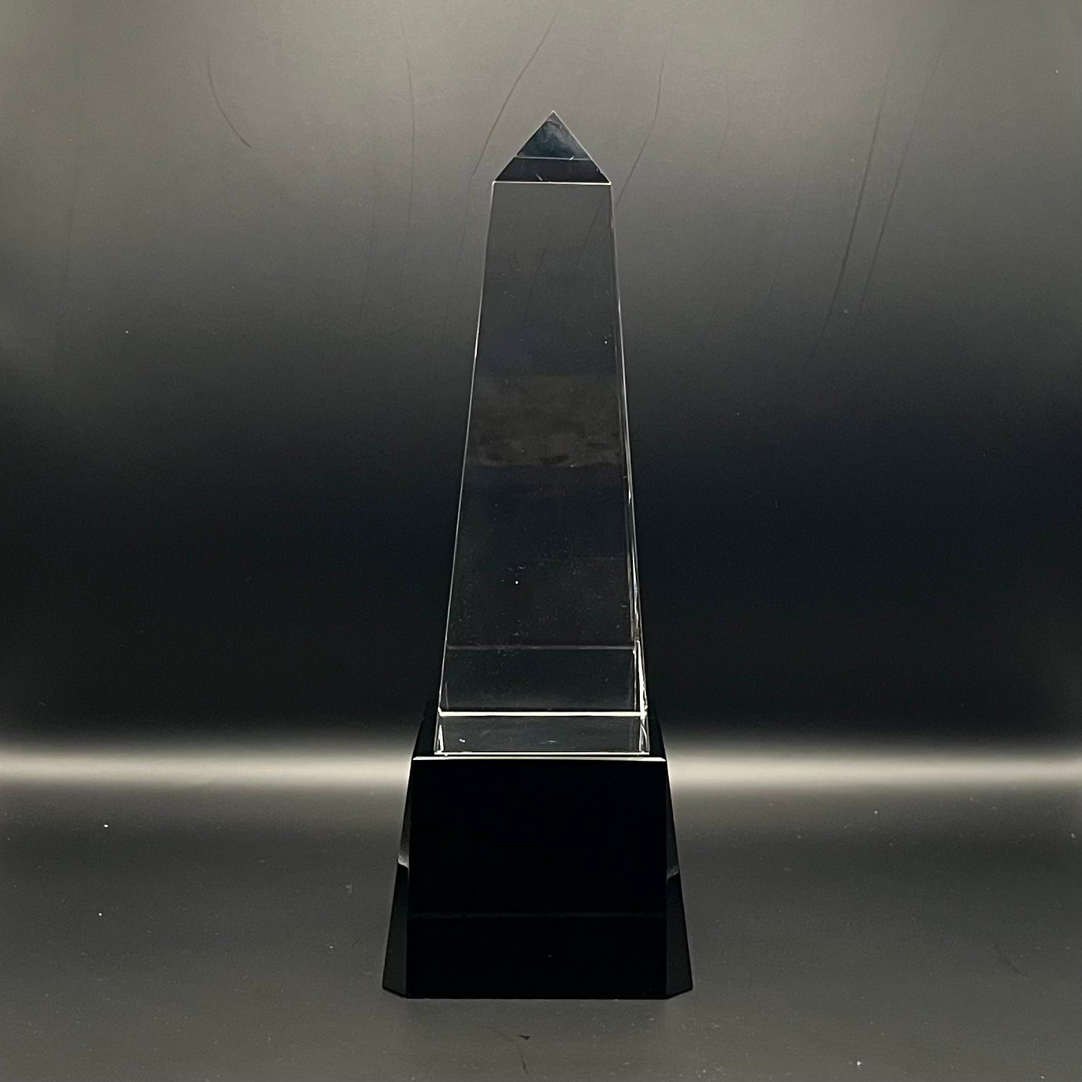 Clear crystal obelisk on a black base against a dark background