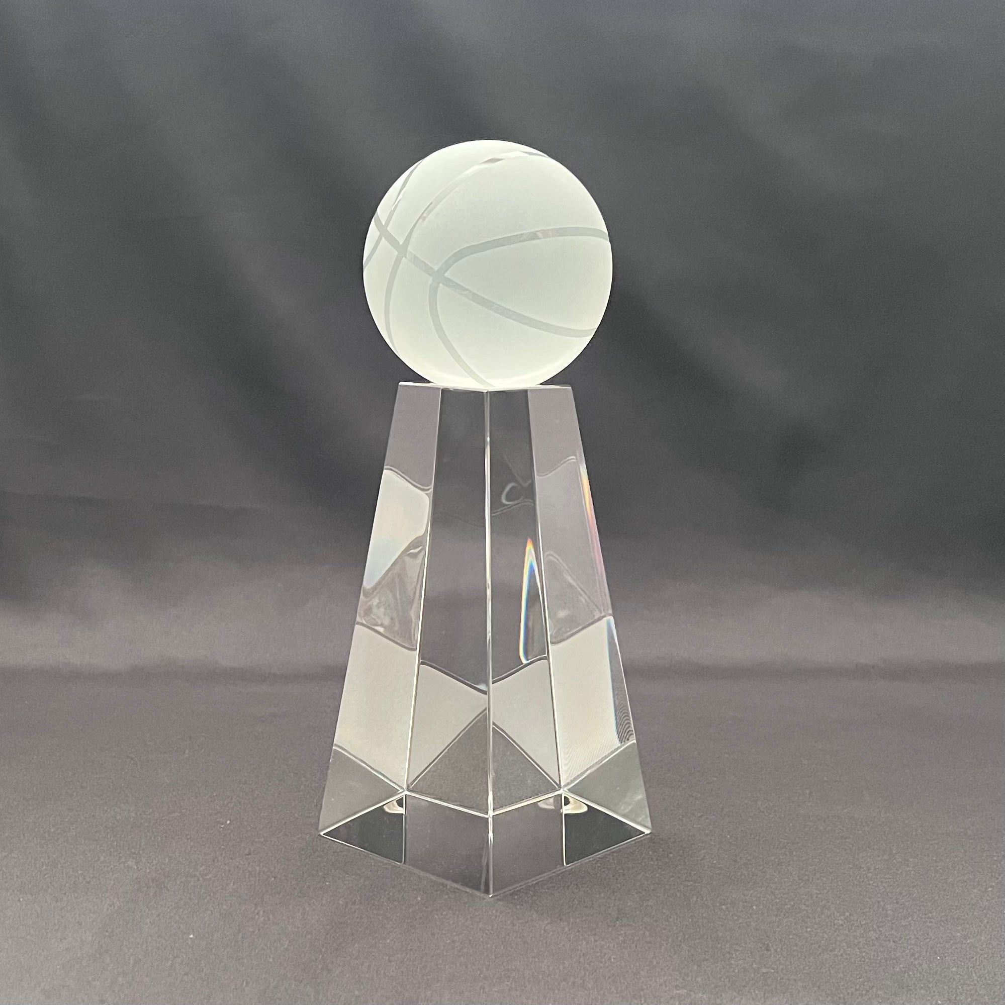 A clear acrylic crystal trophy display stand featuring a faceted geometric base and a frosted white basketball-shaped top.