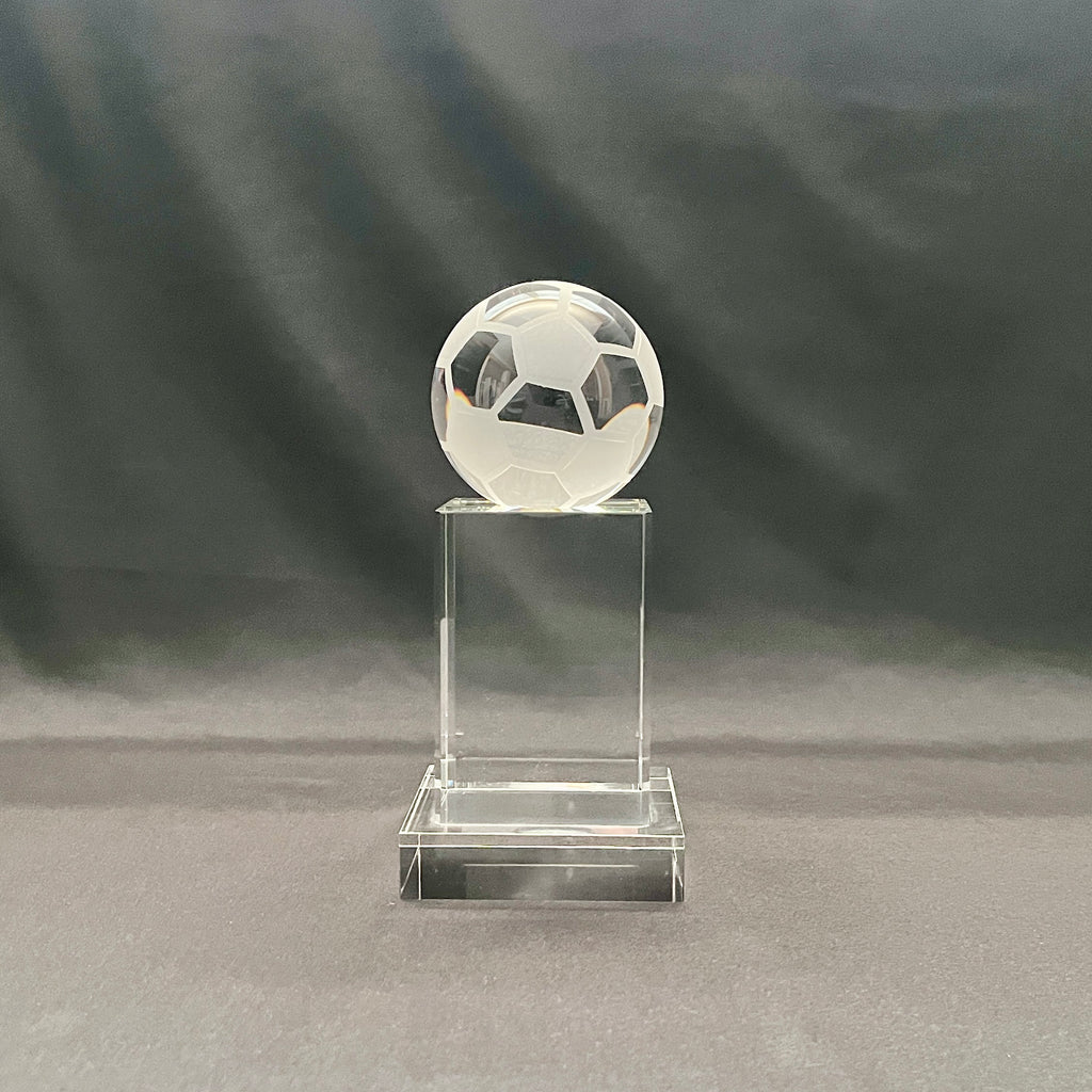A clear crystal trophy stand featuring a soccer ball design on top of a rectangular base