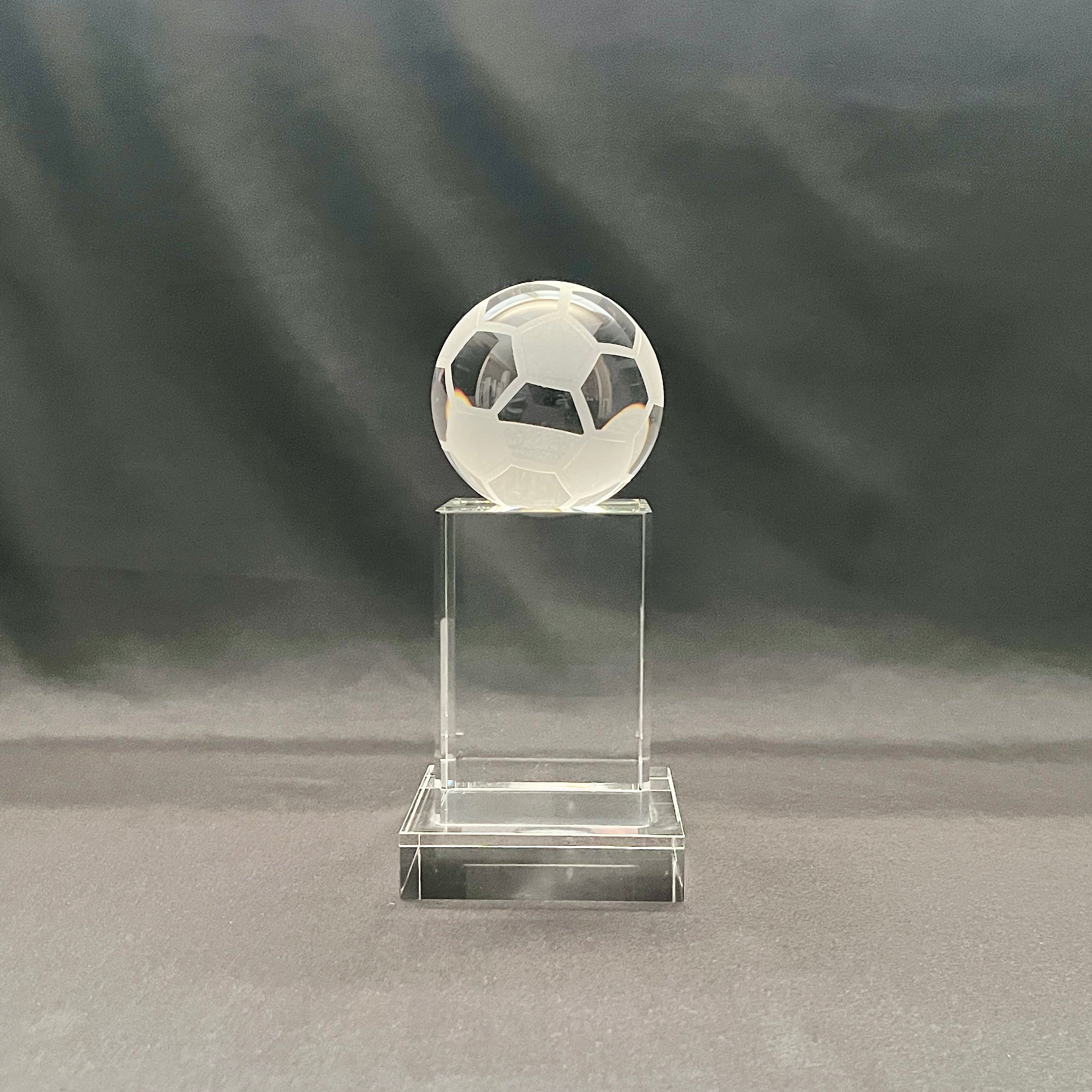 A clear crystal trophy stand featuring a soccer ball design on top of a rectangular base