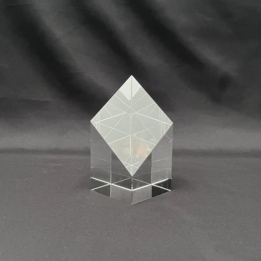 A clear acrylic geometric crystal award block with a diamond-shaped top and a multi-tiered base, 