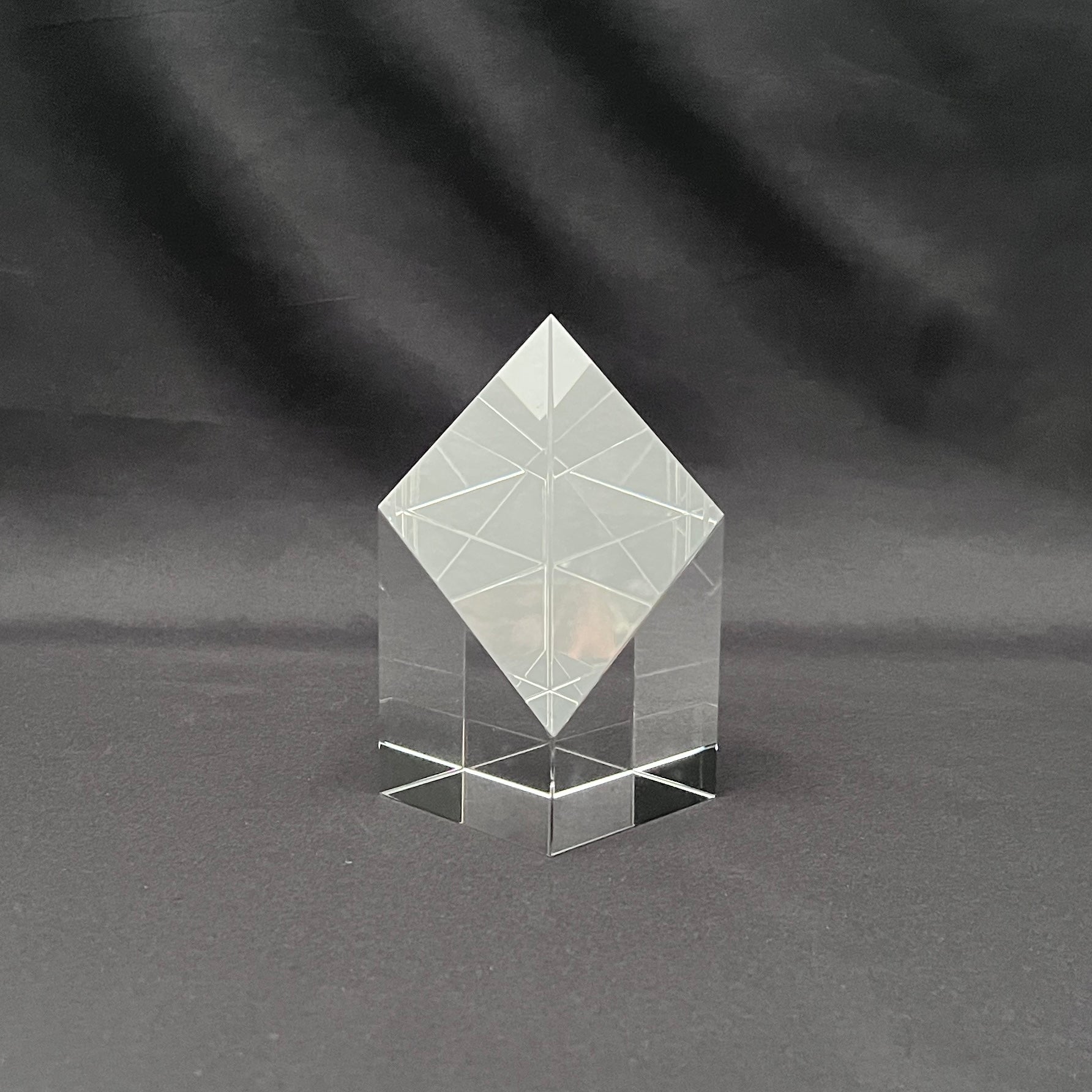A clear acrylic geometric crystal award block with a diamond-shaped top and a multi-tiered base, 