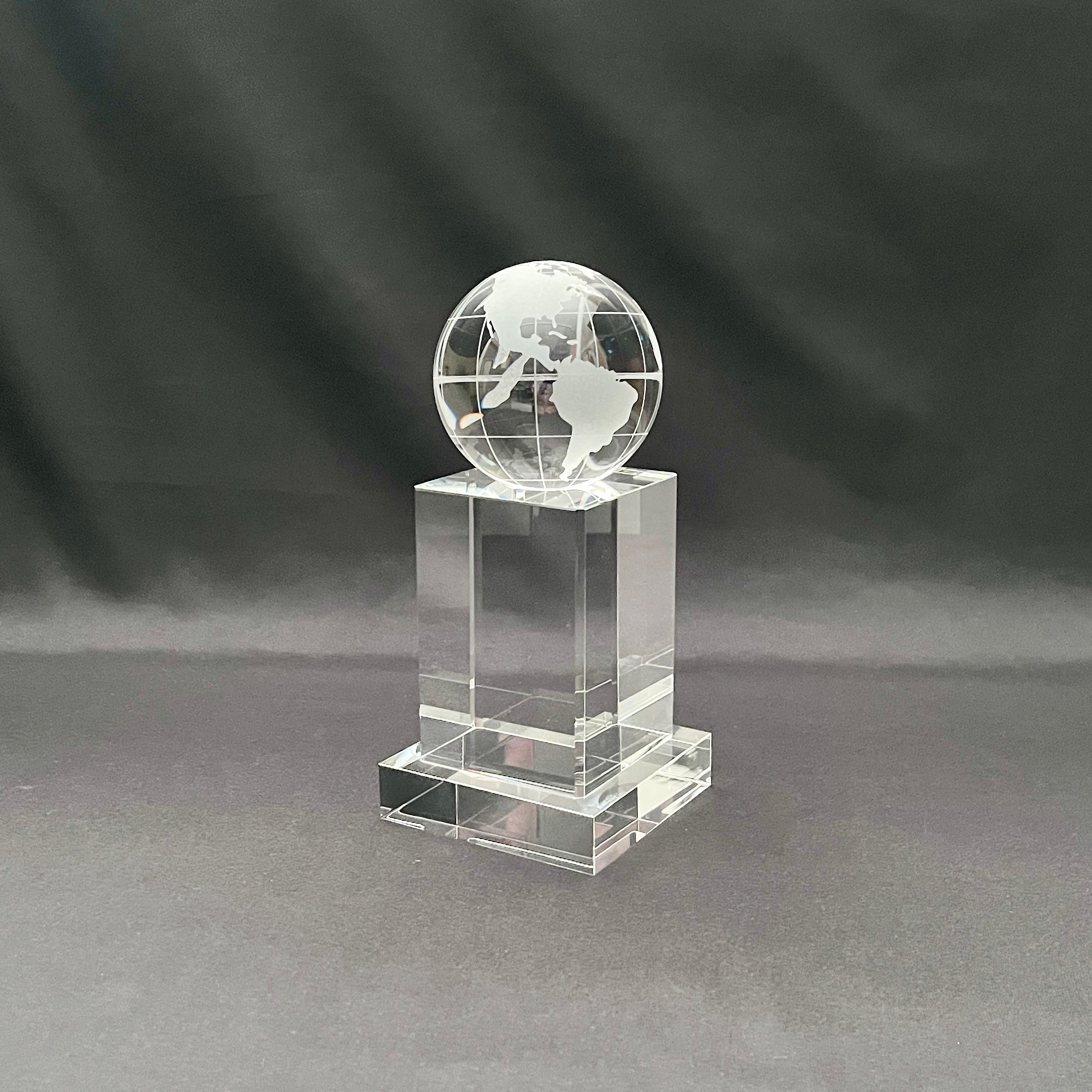 A clear acrylic or glass trophy featuring an etched globe on top of a rectangular pedestal base.