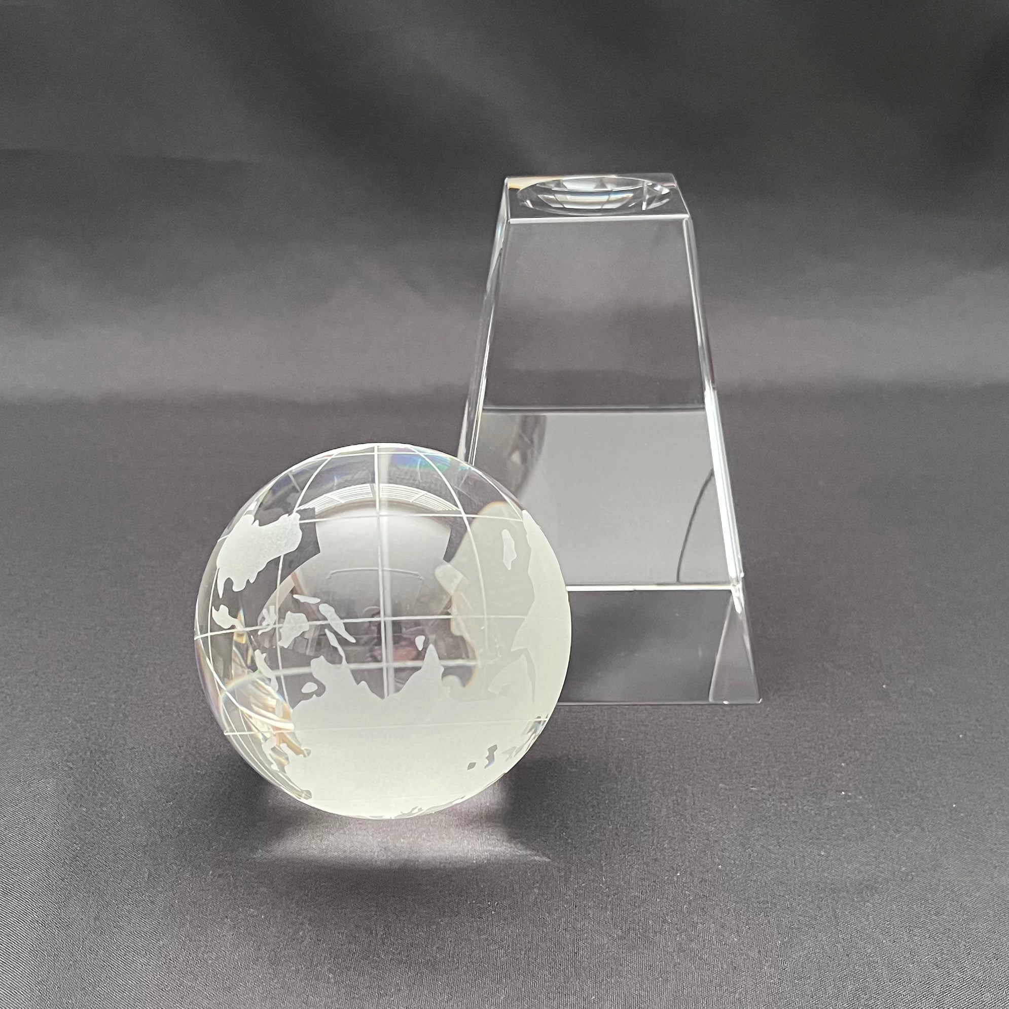 A clear glass globe desk ornament with an etched world map design, shown next to its transparent acrylic display stand