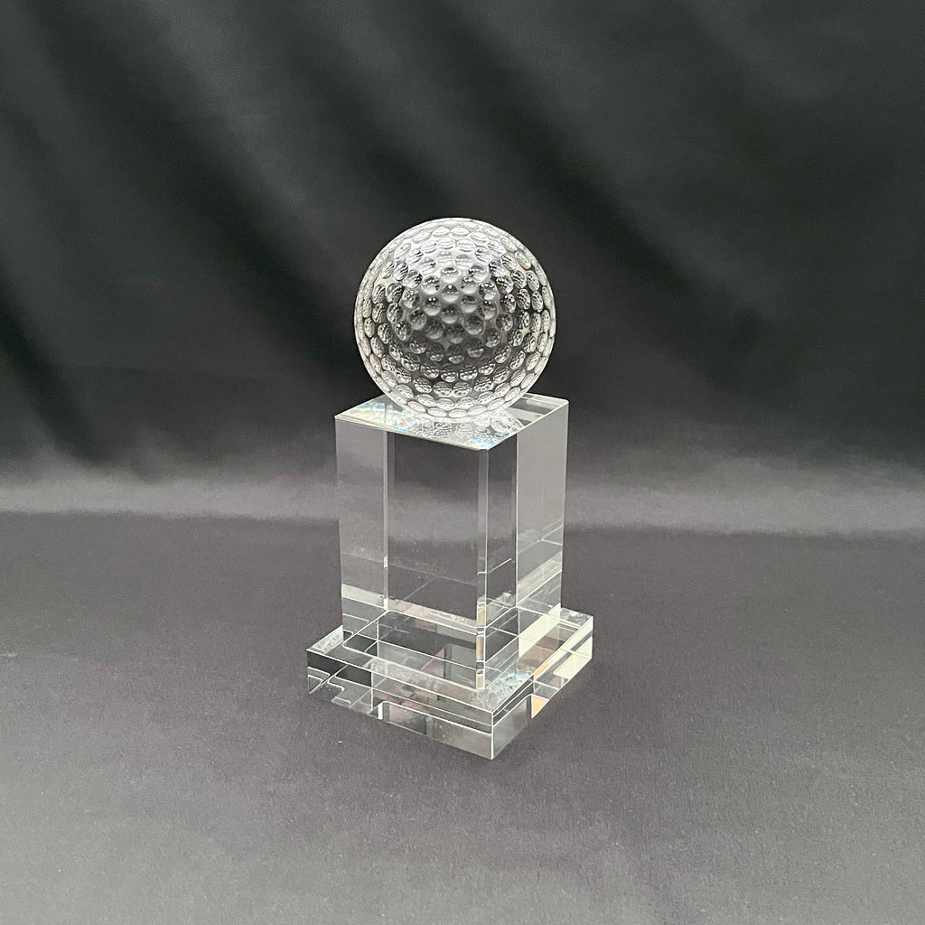 A clear crystal trophy stand featuring a textured, dimpled golf ball on top