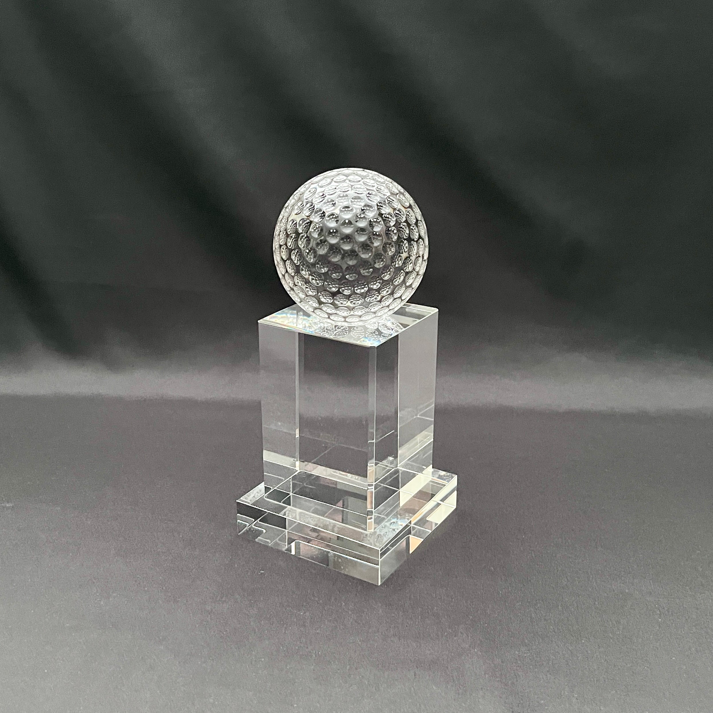 A clear crystal trophy stand featuring a textured, dimpled golf ball on top