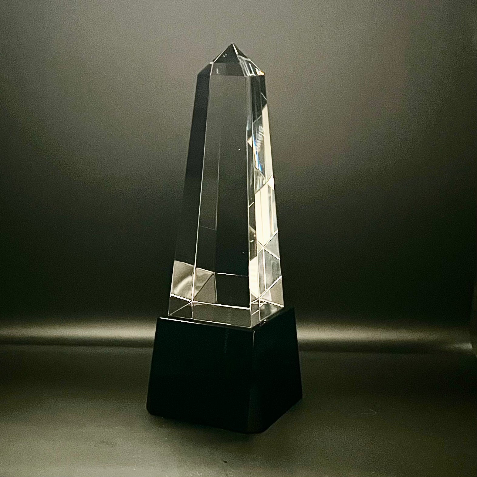 Crystal obelisk on a black base against a dark background