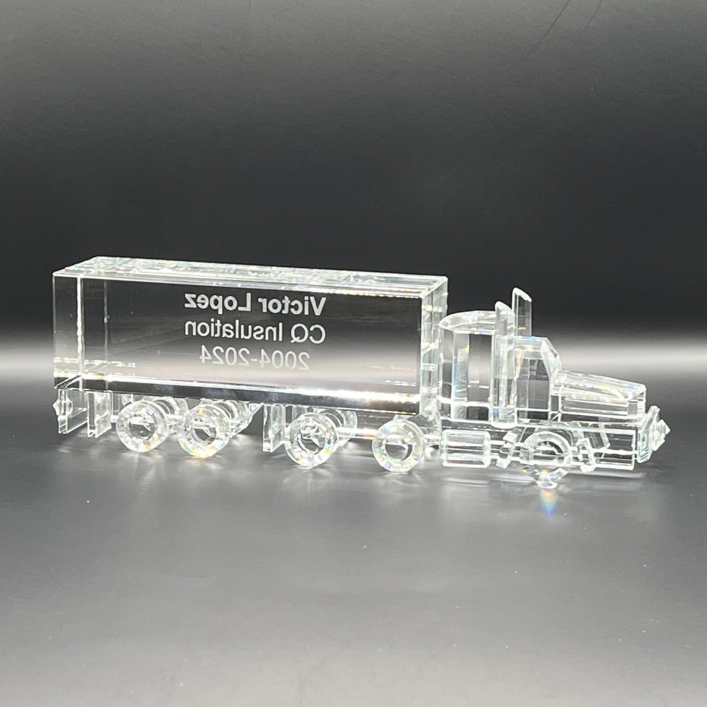 Clear glass model of a truck with engraved text on a dark background