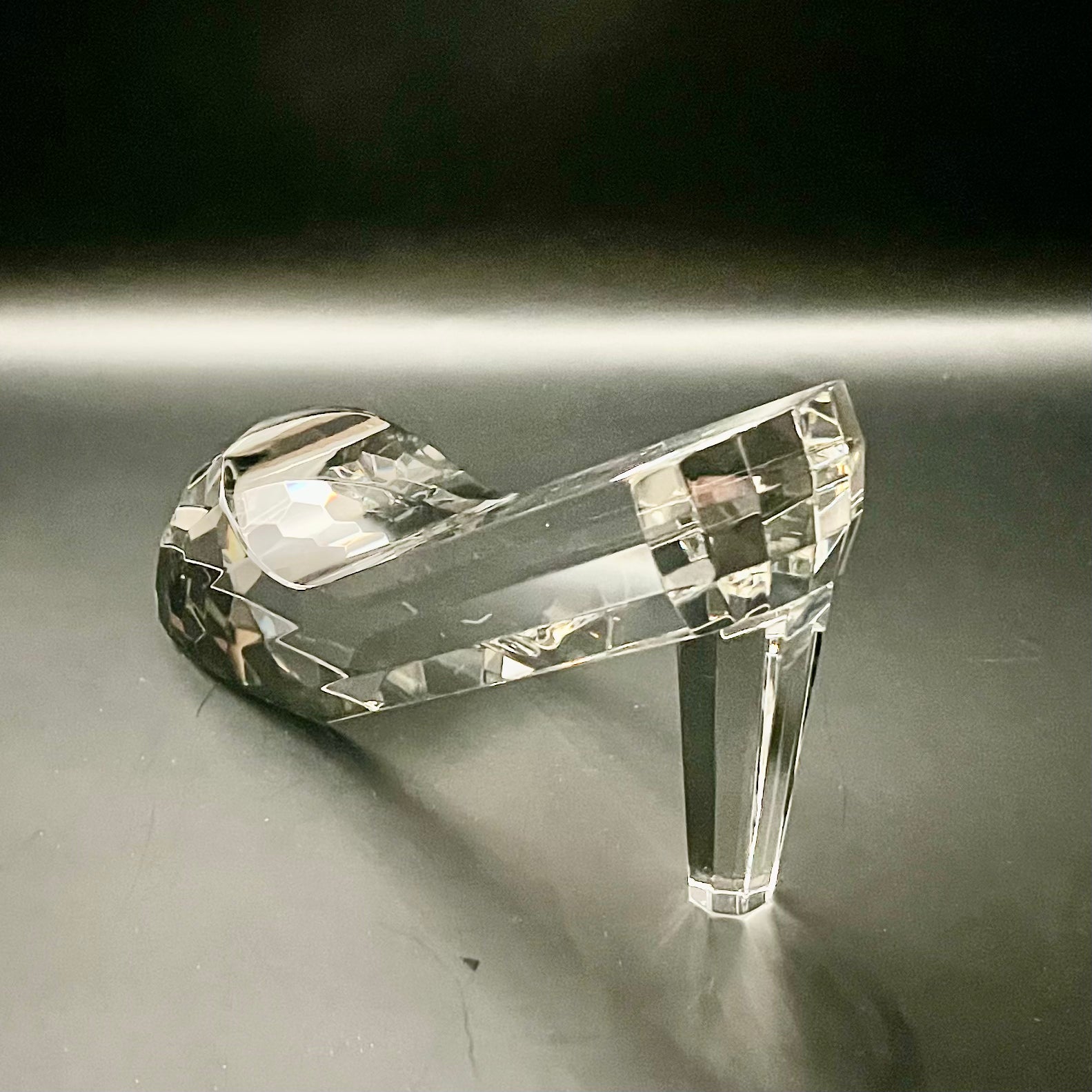 Crystal high-heeled shoe on a reflective surface with a dark background