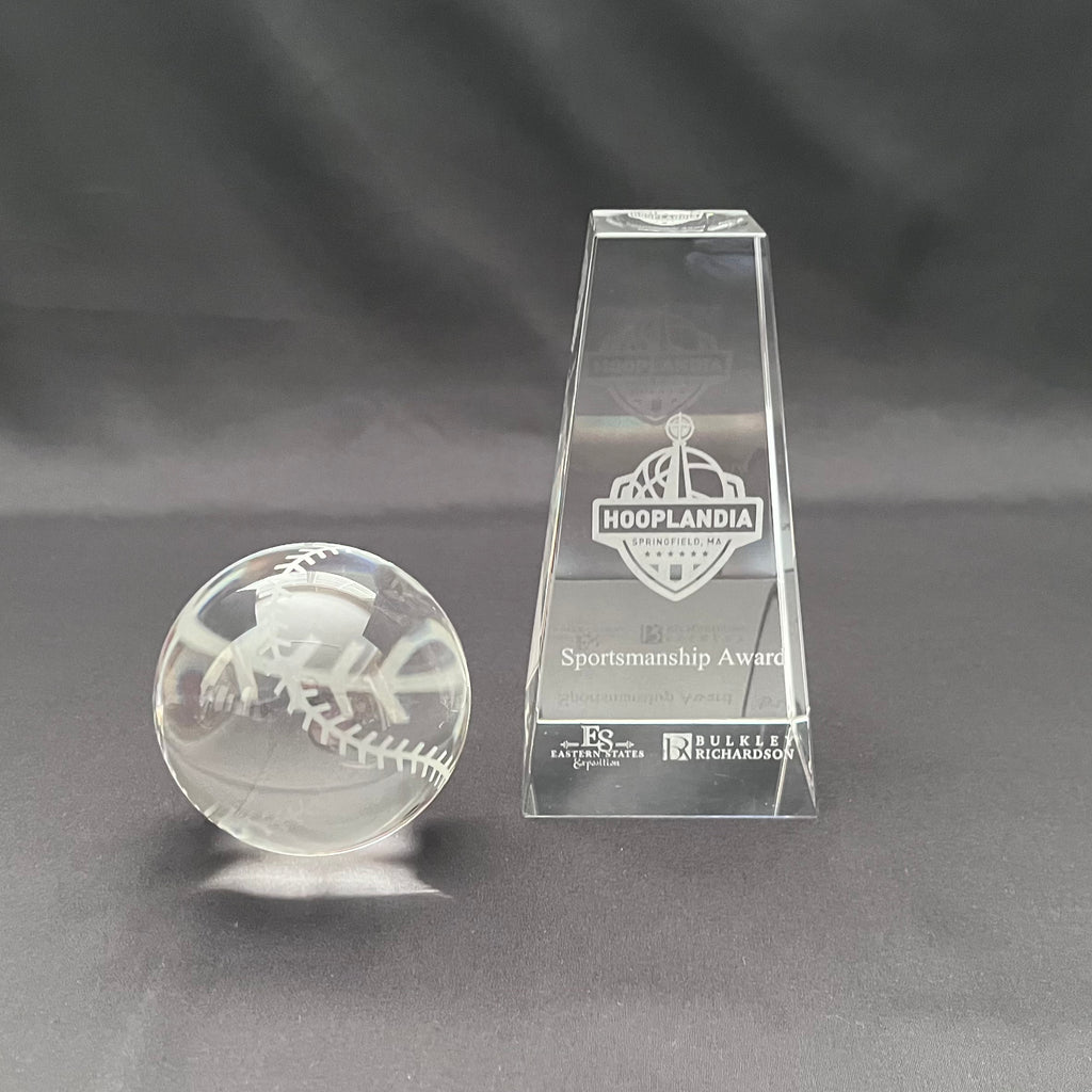 A clear crystal sportsmanship award trophy set on a dark gray background, featuring a tall rectangular base engraved with logo and text 