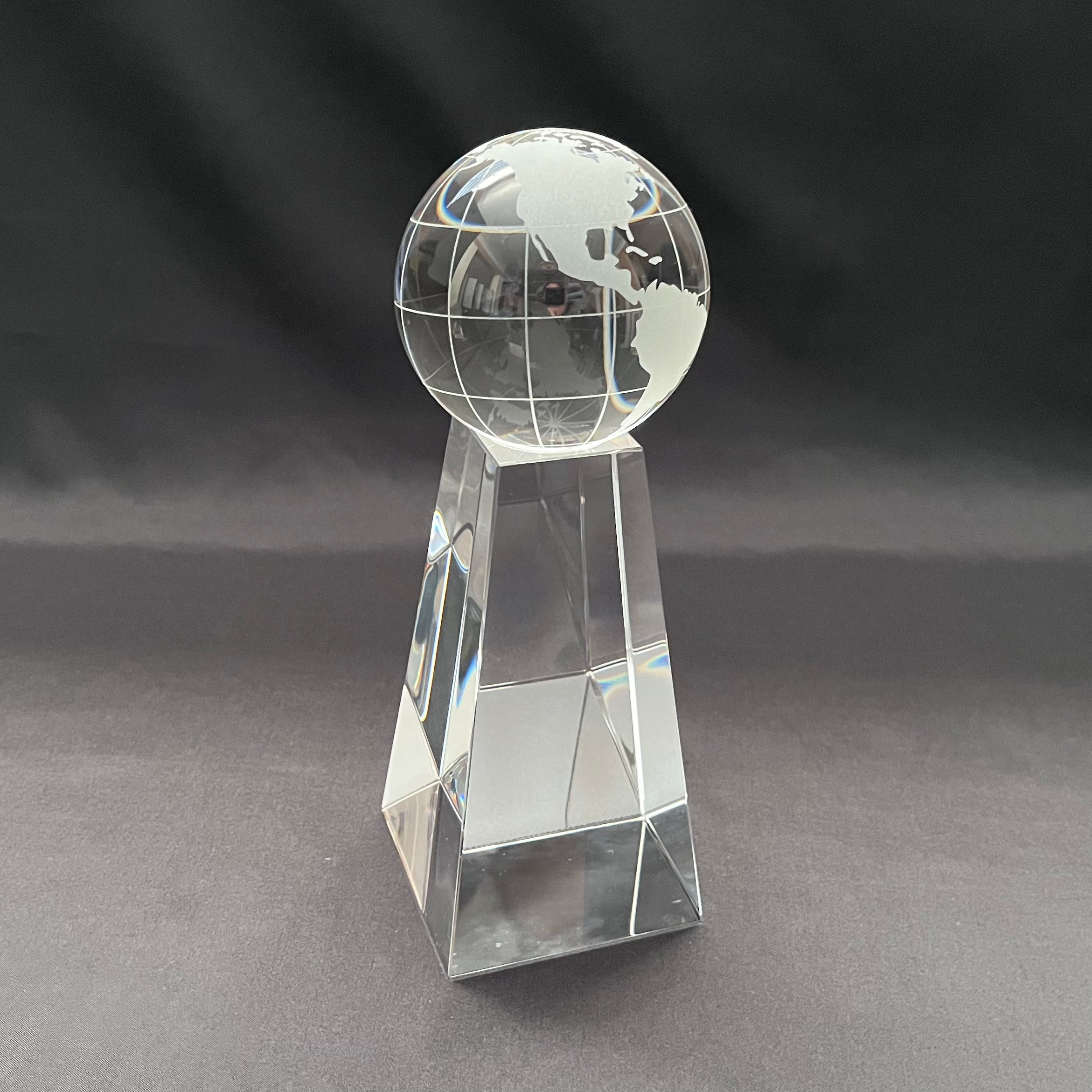 A clear glass or acrylic trophy-style globe on a faceted rectangular pedestal, 
