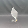 A clear acrylic or glass geometric crystal award block with a faceted diamond-like top, standing on a gray fabric background.