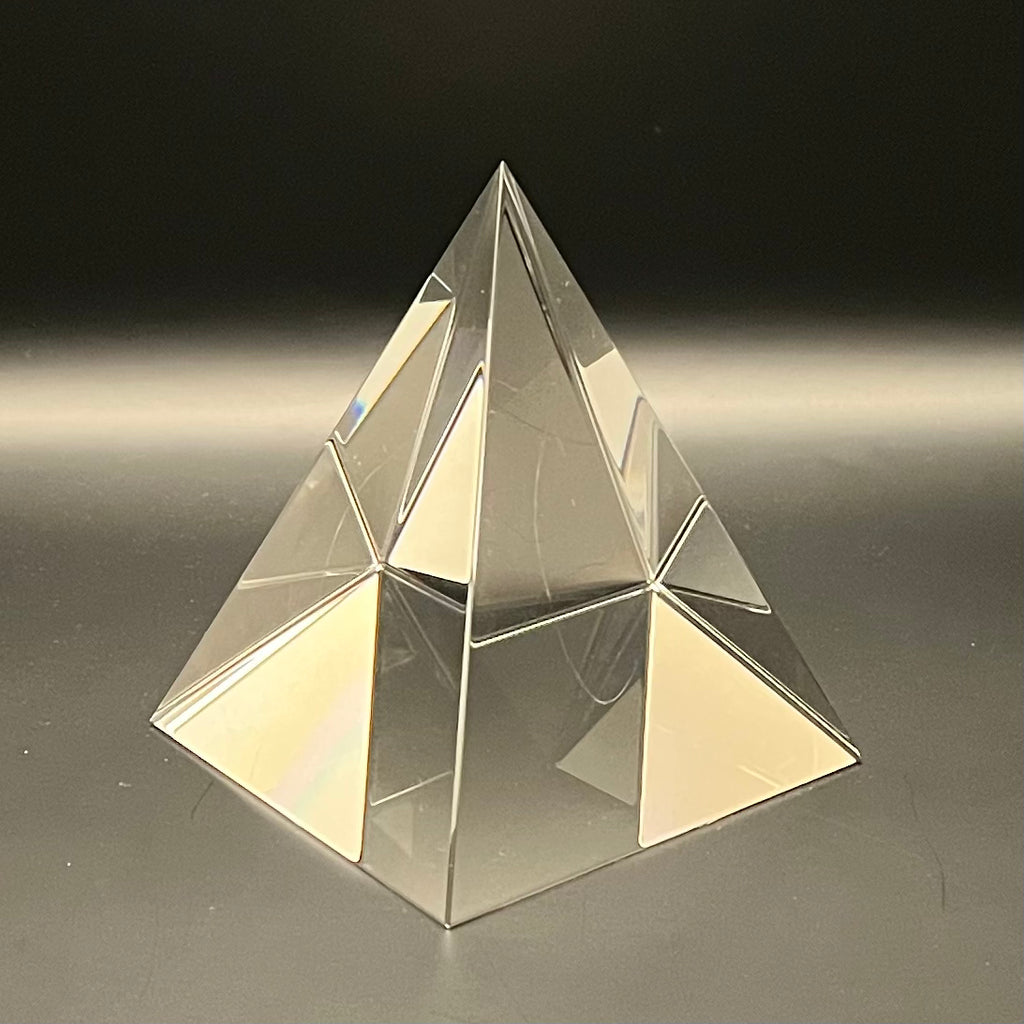 Clear pyramid-shaped object on a reflective surface with a dark background