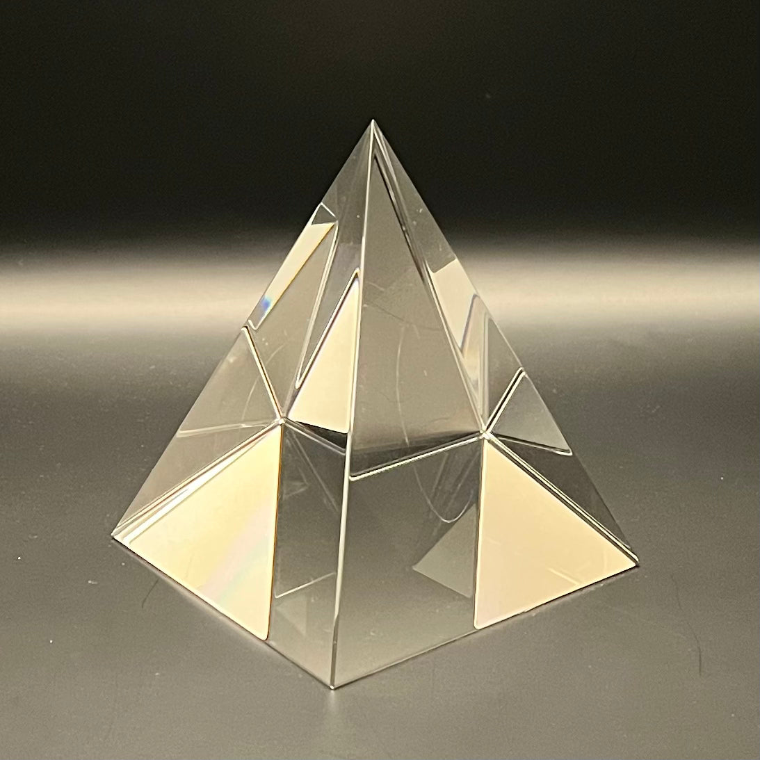 Clear pyramid-shaped object on a reflective surface with a dark background