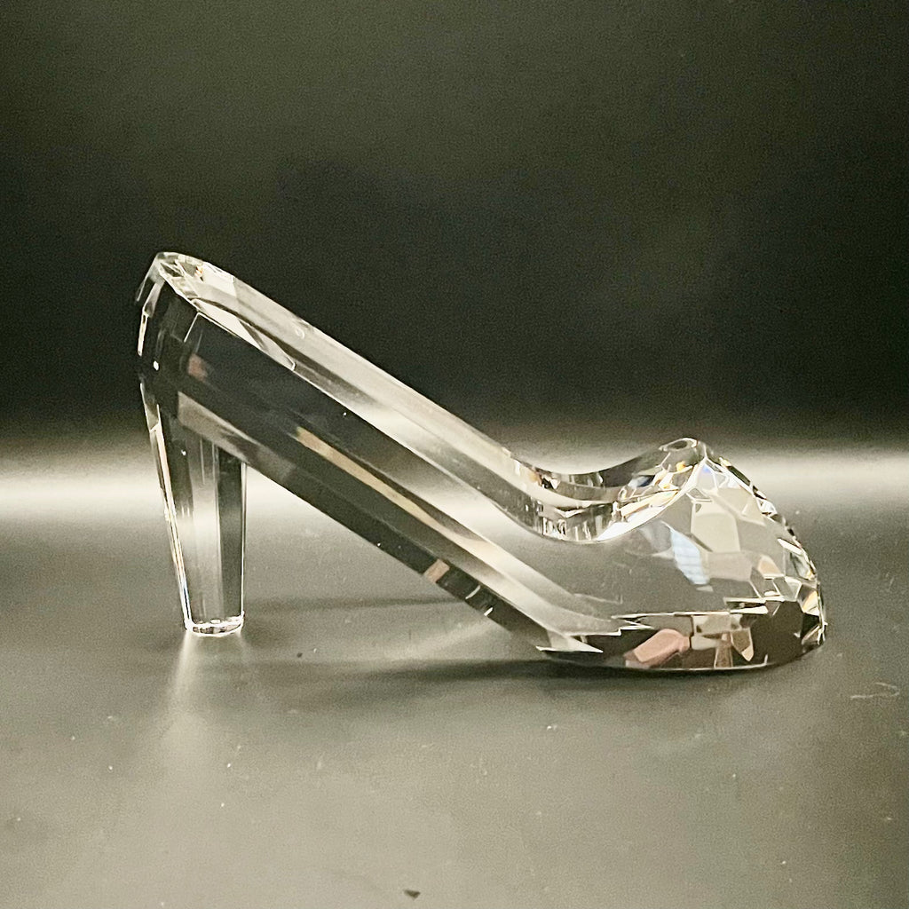 Clear glass high-heeled shoe on a reflective surface with a dark background