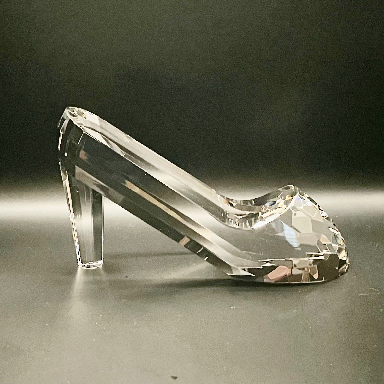 Clear glass high-heeled shoe on a reflective surface with a dark background