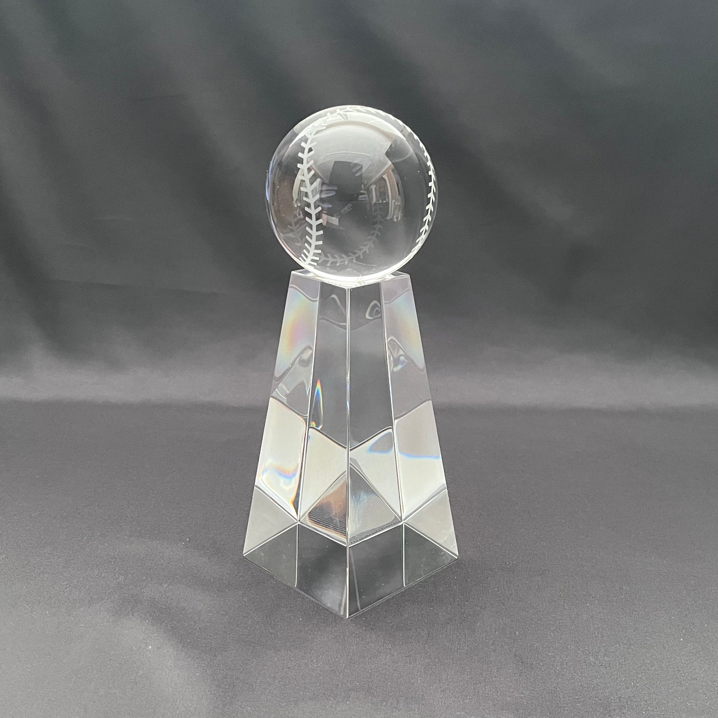 A clear glass trophy featuring a baseball engraved on the top sphere, mounted on a faceted geometric pedestal.